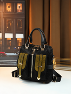 A black textured handbag with gold-tone hardware and two prominent gold textured front straps, displayed on a white surface with a warm-toned background.