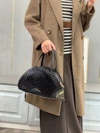 Person wearing a brown coat holding a black handbag in front of a mirror.