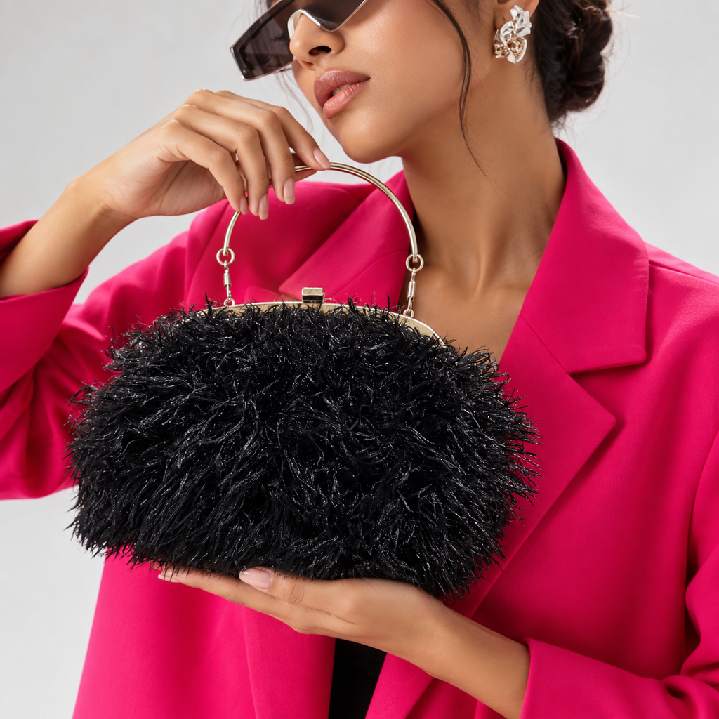 A woman in a bright pink blazer holds a black feathered handbag with a gold-tone metal handle and frame against a light gray studio background.